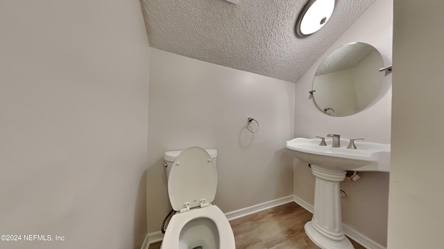 bathroom with vaulted ceiling, toilet, wood-type flooring, and a textured ceiling