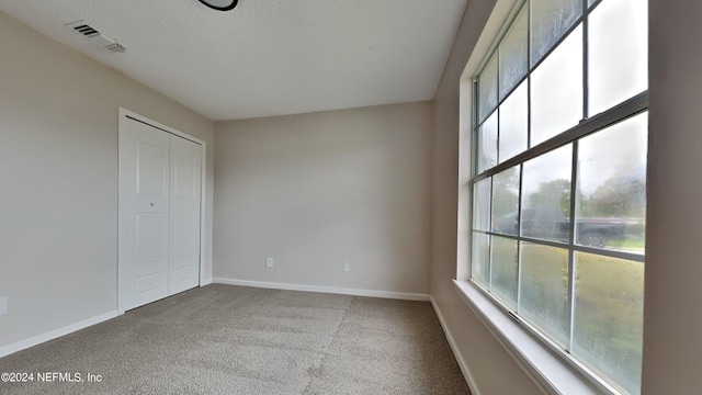 carpeted empty room with visible vents, a textured ceiling, and baseboards