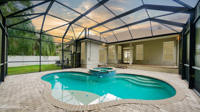 pool at dusk with an in ground hot tub, a patio, and a lanai