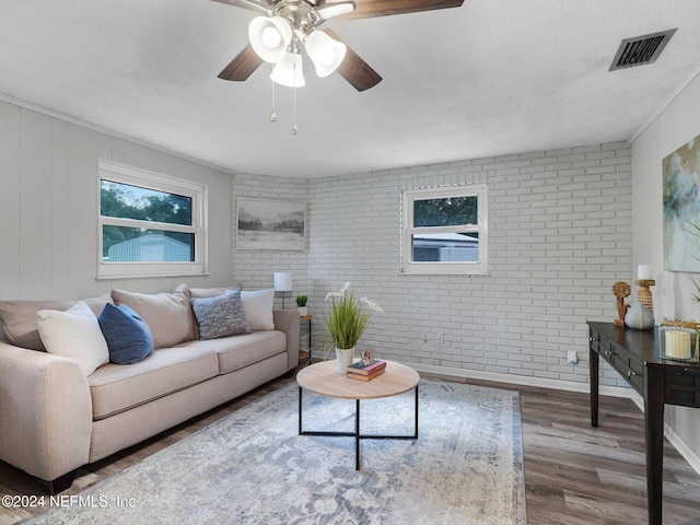 living room with ceiling fan, wood-type flooring, brick wall, and ornamental molding