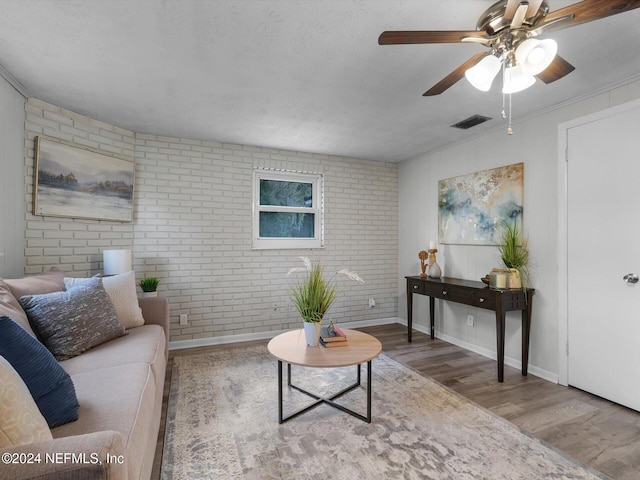 living room featuring wood-type flooring, ornamental molding, a textured ceiling, ceiling fan, and brick wall