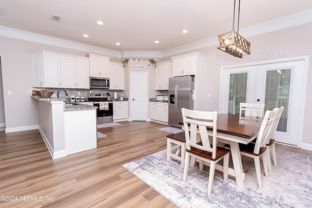 kitchen featuring pendant lighting, white cabinetry, appliances with stainless steel finishes, light stone counters, and light hardwood / wood-style floors