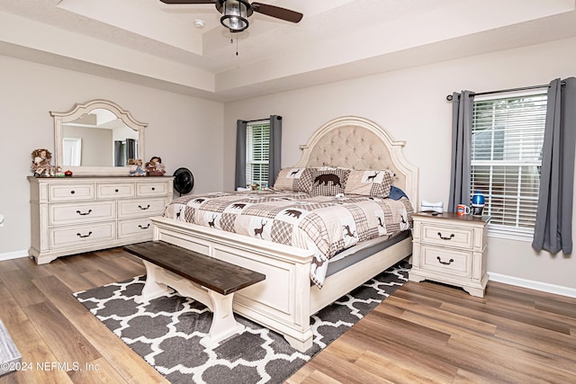 bedroom with ceiling fan, a raised ceiling, and dark hardwood / wood-style flooring