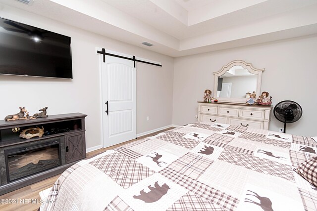 bedroom featuring a barn door, light hardwood / wood-style floors, and a raised ceiling