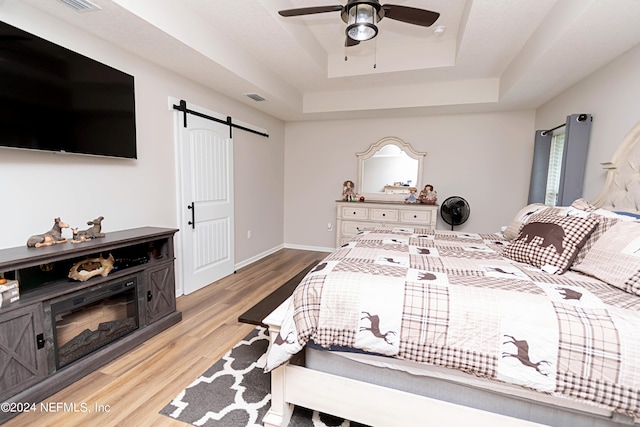 bedroom featuring light hardwood / wood-style flooring, a barn door, a tray ceiling, and ceiling fan