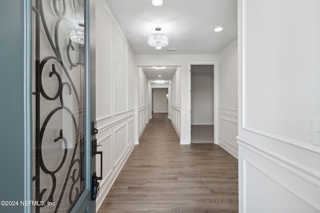 hall featuring recessed lighting, light wood-style floors, a decorative wall, and a notable chandelier