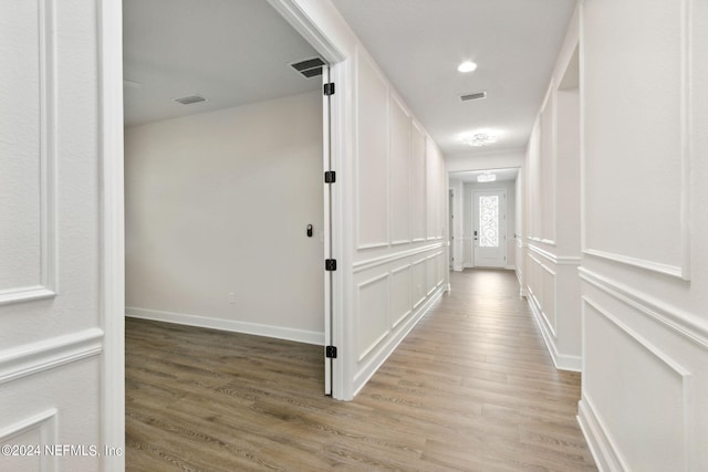 hall with a decorative wall, light wood-style floors, visible vents, and baseboards