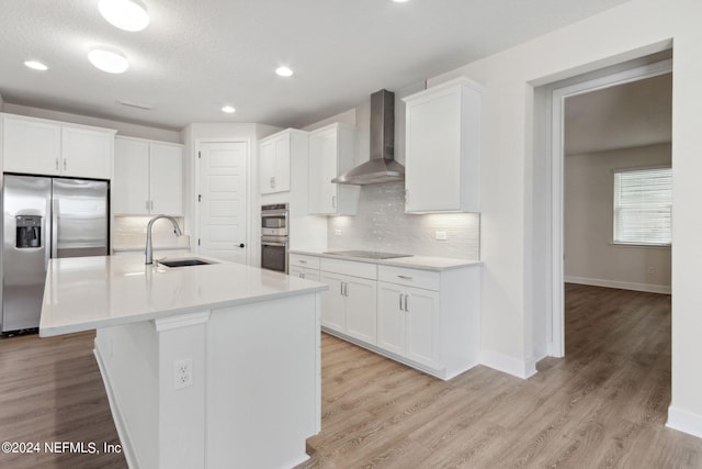 kitchen featuring white cabinets, stainless steel appliances, wall chimney range hood, a sink, and tasteful backsplash