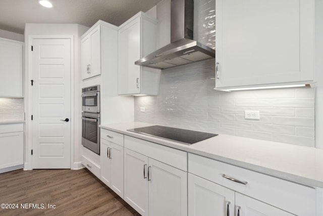 kitchen with white cabinets, stainless steel double oven, wall chimney range hood, black electric stovetop, and light countertops