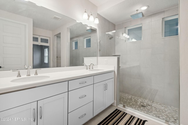 bathroom with tile patterned flooring, a textured ceiling, vanity, and tiled shower