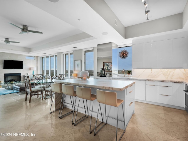 kitchen featuring ceiling fan, a tray ceiling, a kitchen bar, a center island, and white cabinetry