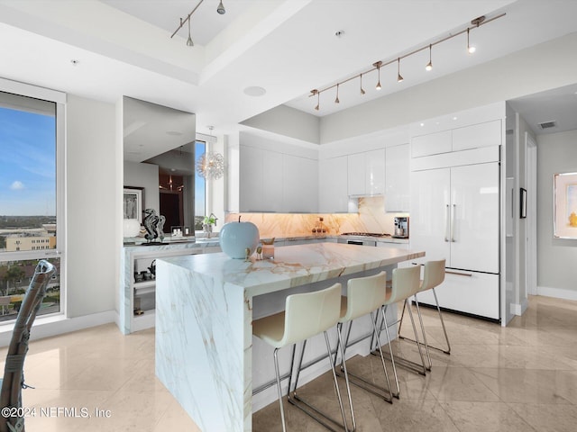 kitchen with paneled fridge, tasteful backsplash, a kitchen island, a breakfast bar, and white cabinets