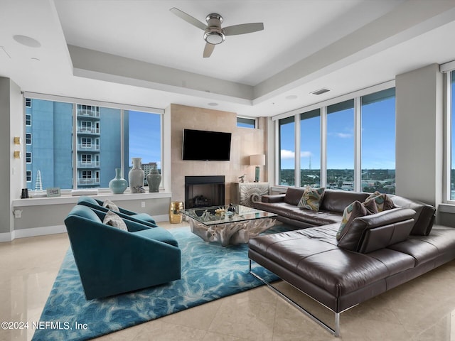 living room featuring expansive windows, ceiling fan, a tray ceiling, and a large fireplace