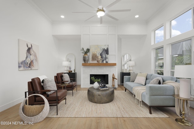 living room featuring light hardwood / wood-style flooring, ornamental molding, a fireplace, a towering ceiling, and ceiling fan