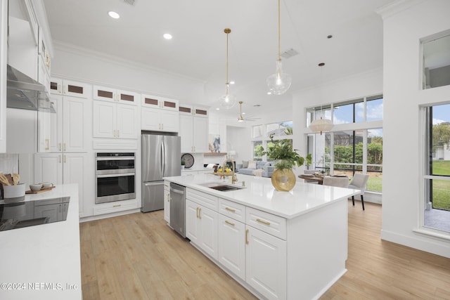 kitchen featuring a kitchen island with sink, stainless steel appliances, sink, decorative light fixtures, and white cabinetry