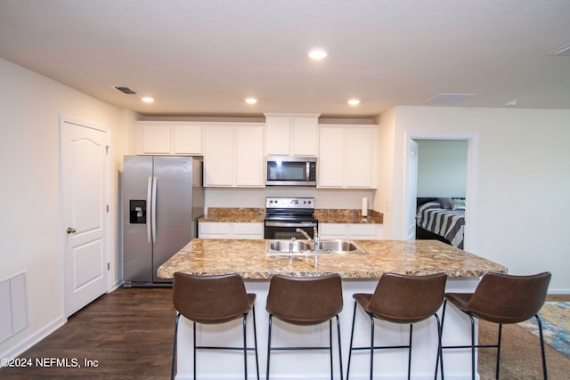 kitchen with a center island with sink, appliances with stainless steel finishes, dark wood-type flooring, and white cabinetry