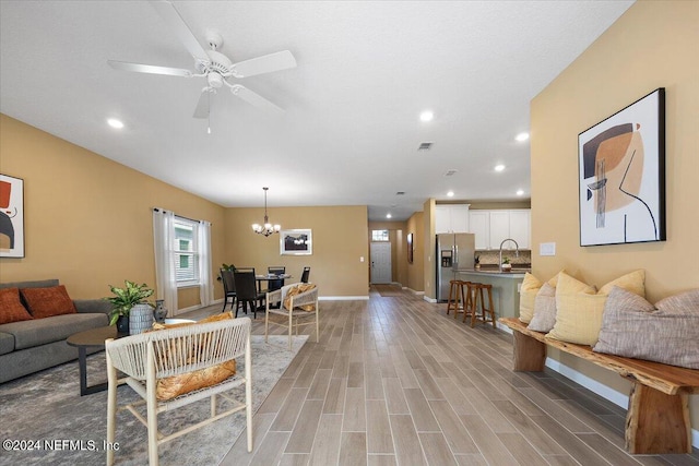 living room with hardwood / wood-style floors, ceiling fan with notable chandelier, and sink