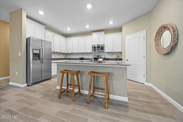 kitchen featuring backsplash, white cabinets, an island with sink, appliances with stainless steel finishes, and light hardwood / wood-style floors