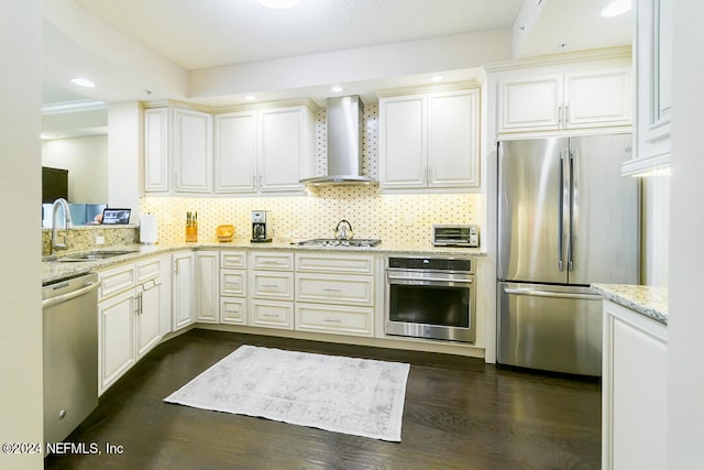 kitchen featuring wall chimney range hood, dark wood-type flooring, stainless steel appliances, sink, and white cabinetry