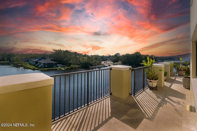 balcony at dusk featuring a water view