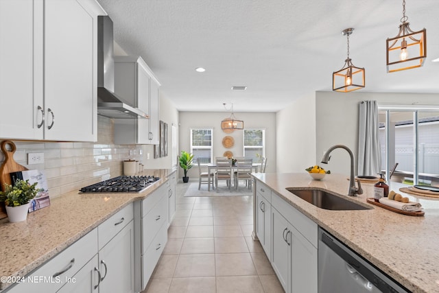 kitchen with wall chimney exhaust hood, decorative light fixtures, sink, and stainless steel appliances