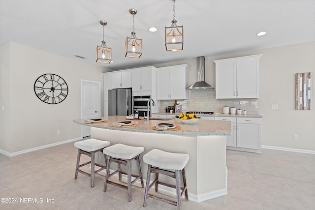 kitchen with white cabinets, an island with sink, wall chimney exhaust hood, and stainless steel appliances