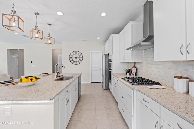 kitchen featuring wall chimney exhaust hood, sink, stainless steel appliances, an island with sink, and white cabinets