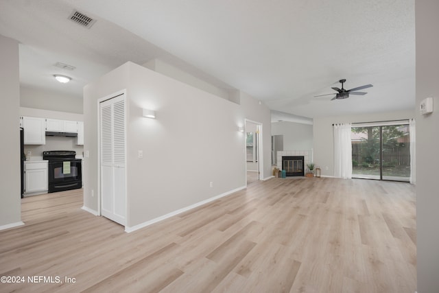 unfurnished living room with a textured ceiling, light hardwood / wood-style floors, ceiling fan, and a tiled fireplace