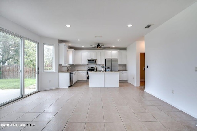 kitchen with appliances with stainless steel finishes, sink, light tile patterned floors, a center island, and white cabinetry