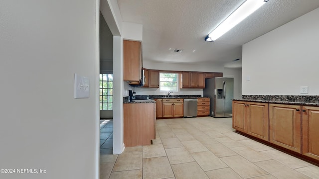 kitchen featuring dark stone countertops, a textured ceiling, appliances with stainless steel finishes, and light tile patterned floors