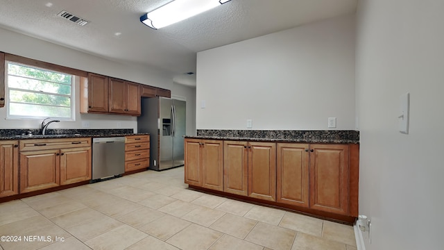 kitchen with dark stone countertops, a textured ceiling, stainless steel appliances, and light tile patterned floors