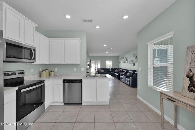 kitchen with stainless steel appliances, sink, light tile patterned flooring, kitchen peninsula, and white cabinetry