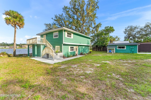 back of property with a lawn, a deck with water view, and an outdoor structure