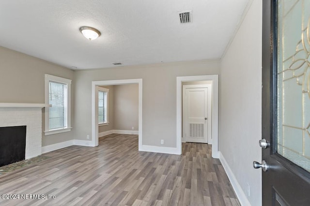 unfurnished living room featuring a fireplace, light hardwood / wood-style floors, crown molding, and a textured ceiling