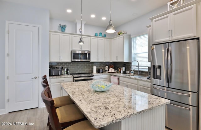 kitchen featuring white cabinets, pendant lighting, appliances with stainless steel finishes, a center island, and light hardwood / wood-style floors