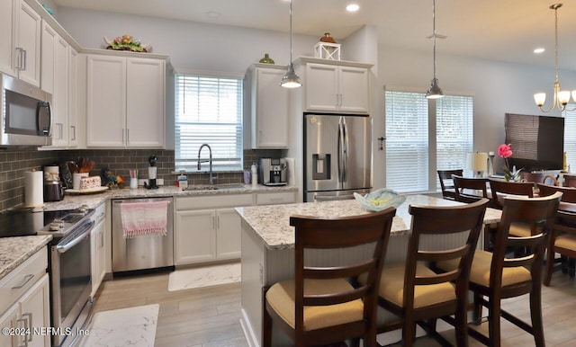 kitchen with light wood-type flooring, pendant lighting, a kitchen island, stainless steel appliances, and white cabinets