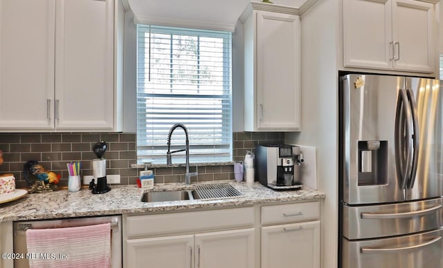 kitchen with sink, light stone counters, stainless steel appliances, backsplash, and white cabinetry