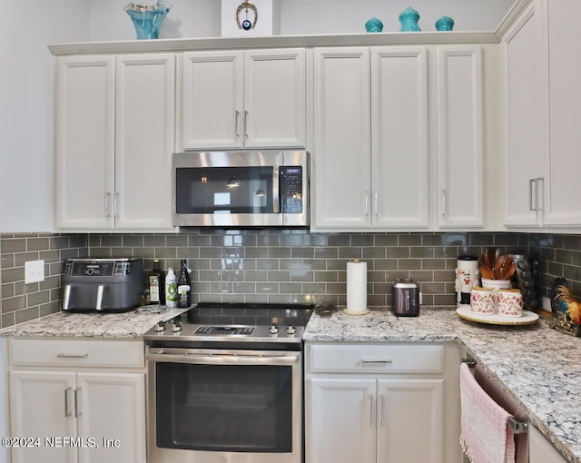 kitchen with stainless steel appliances, light stone countertops, decorative backsplash, and white cabinetry