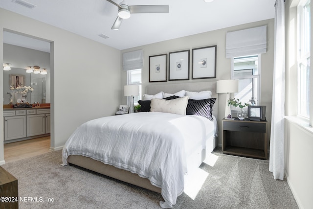 bedroom with ceiling fan, connected bathroom, and light carpet