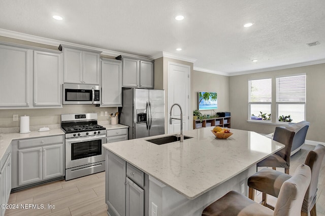 kitchen with stainless steel appliances, a center island with sink, and light stone countertops