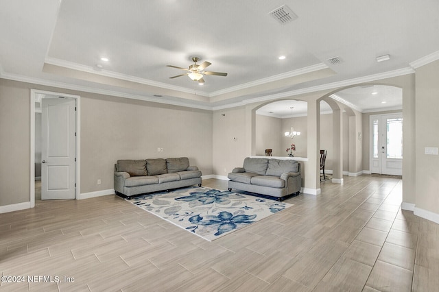 living room featuring a tray ceiling, ornamental molding, and ceiling fan with notable chandelier