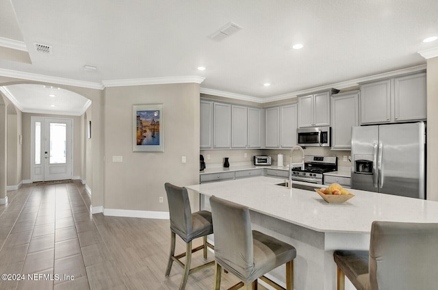 kitchen featuring a kitchen breakfast bar, stainless steel appliances, an island with sink, and light stone countertops