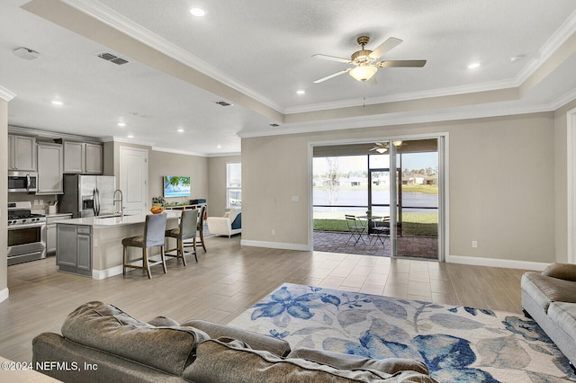 living room with crown molding, sink, a tray ceiling, ceiling fan, and light hardwood / wood-style flooring