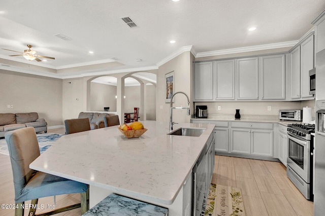 kitchen with a center island with sink, light stone counters, sink, a breakfast bar, and appliances with stainless steel finishes