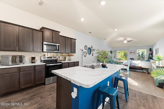 kitchen with a center island with sink, appliances with stainless steel finishes, a breakfast bar, dark hardwood / wood-style floors, and sink