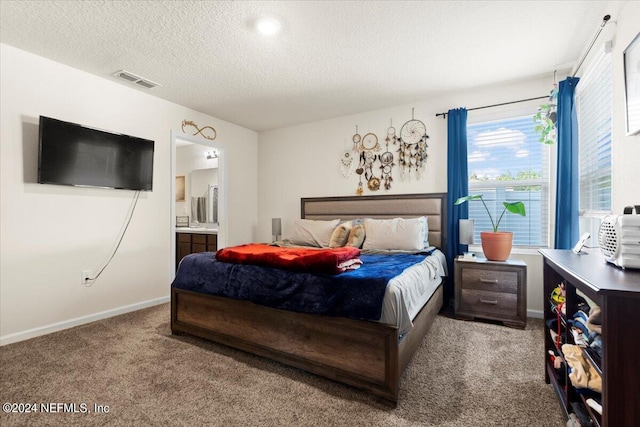 bedroom with ensuite bath, light carpet, and a textured ceiling