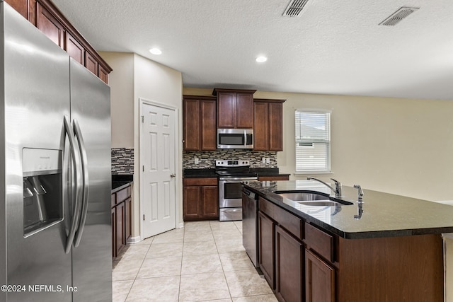 kitchen with stainless steel appliances, a center island with sink, a textured ceiling, sink, and light tile patterned flooring