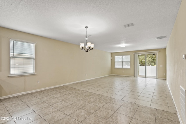 tiled empty room with a textured ceiling and a notable chandelier