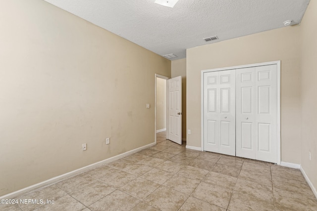 unfurnished bedroom with a textured ceiling, light tile patterned floors, and a closet