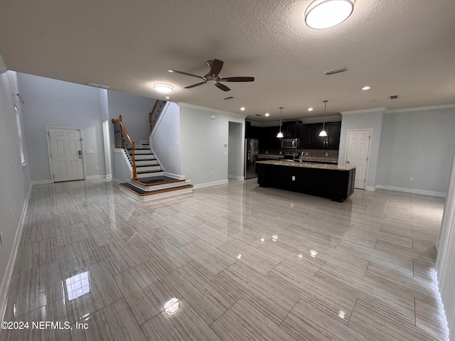 unfurnished living room featuring ceiling fan, sink, light tile patterned flooring, ornamental molding, and a textured ceiling